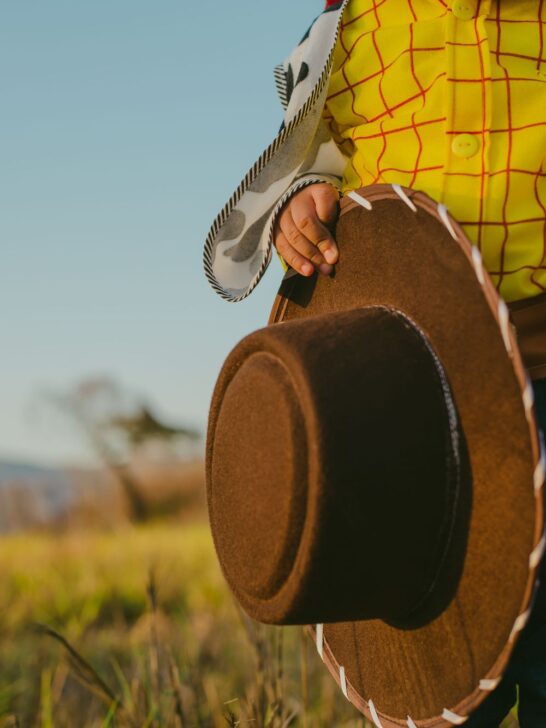 Close-up of a child dressed as Woody holding a cowboy hat while wearing the iconic Toy Story costume