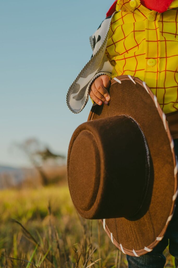 Close-up of a child dressed as Woody holding a cowboy hat while wearing the iconic Toy Story costume