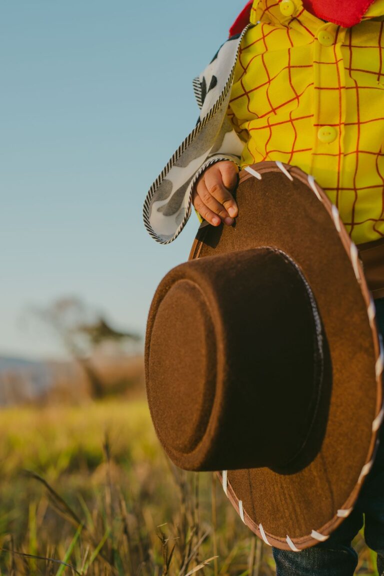 Close-up of a child dressed as Woody holding a cowboy hat while wearing the iconic Toy Story costume
