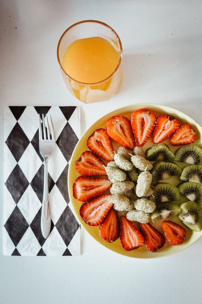 Easy vegan desserts featuring a fresh fruit plate with strawberries, kiwi, white mulberries, and a glass of orange juice.