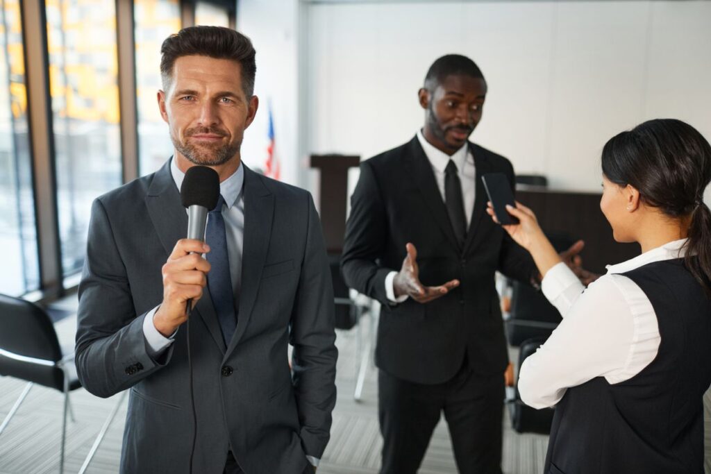 Business keynote speaker holding a microphone at a professional event with attendees in the background