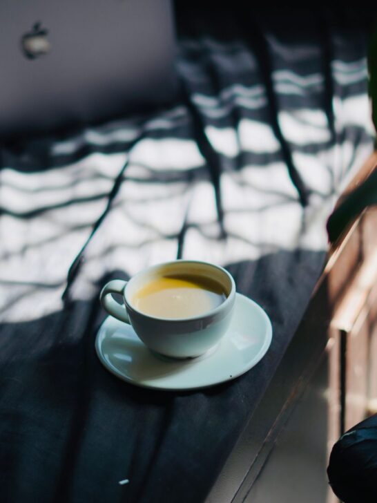 Morning coffee ritual with a white cup of fresh coffee sitting on a windowsill in soft natural light.