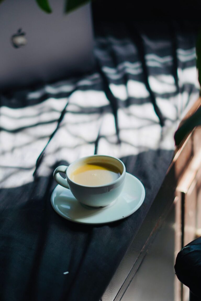 Morning coffee ritual with a white cup of fresh coffee sitting on a windowsill in soft natural light.