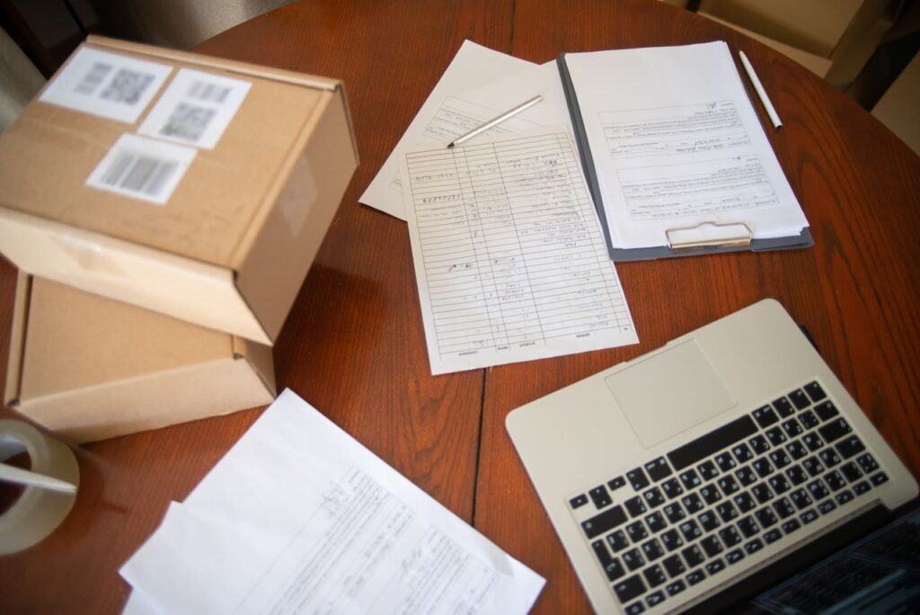 Small business growth paperwork, shipping boxes, and a laptop organized on a desk while preparing business funding documents.