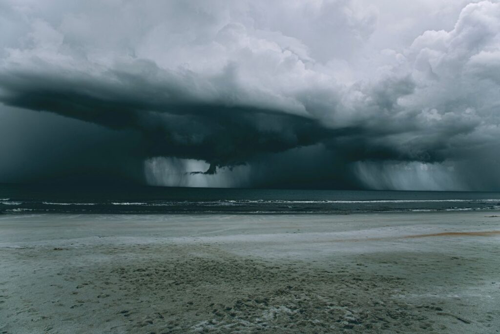 Dark storm clouds and heavy rain moving toward a coastal beach ahead of severe weather.