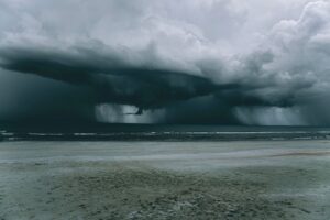 Dark storm clouds and heavy rain moving toward a coastal beach ahead of severe weather.