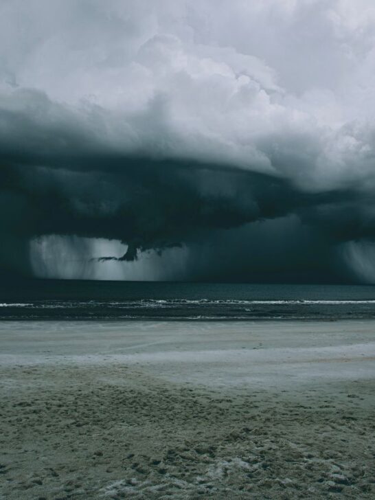 Dark storm clouds and heavy rain moving toward a coastal beach ahead of severe weather.