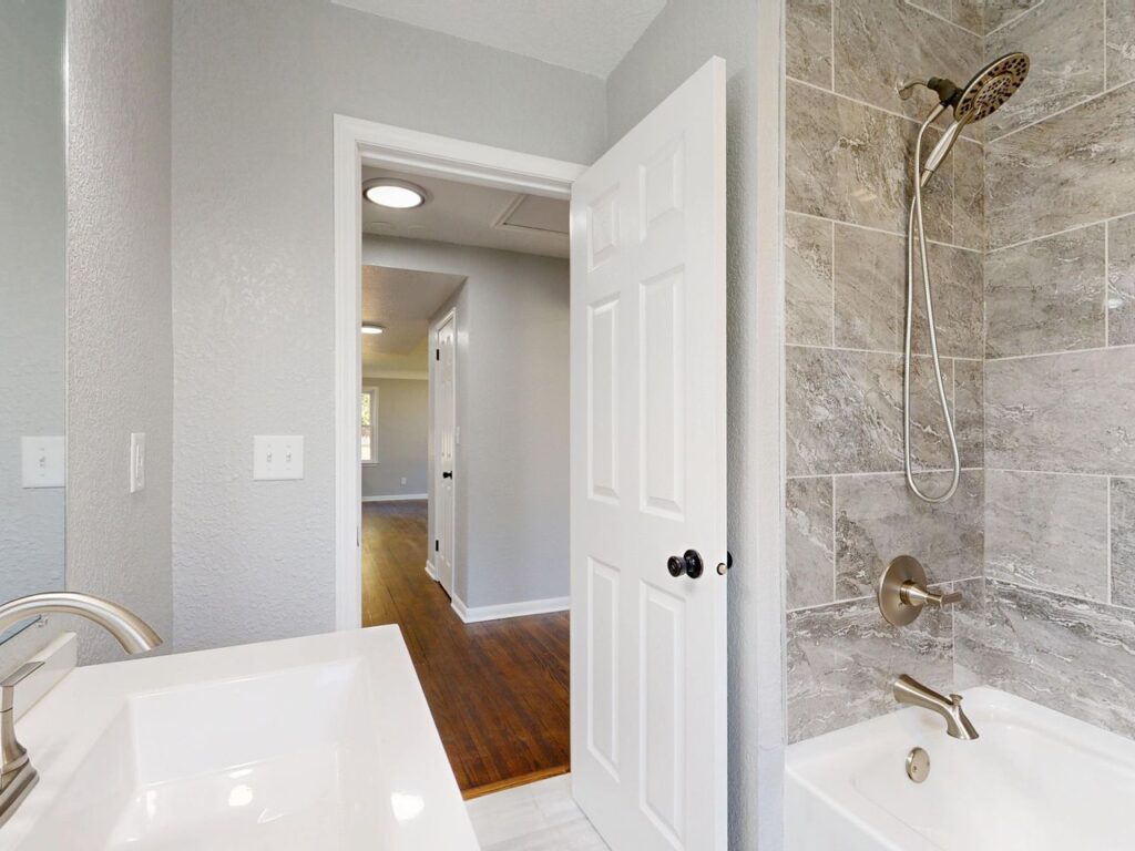 Updated bathroom with a tiled tub and shower combination, handheld showerhead, and modern fixtures.