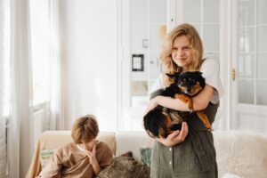 A young girl hugs her small black and brown dog while a boy sits nearby at home.