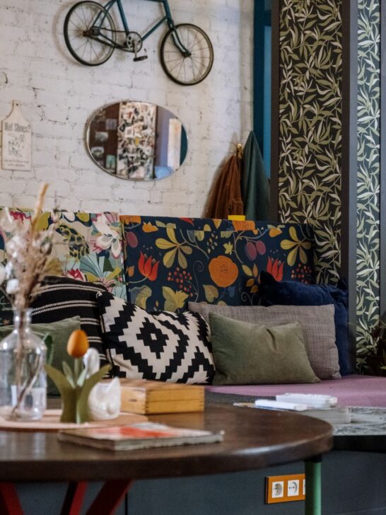 Modern interior with botanical wallpaper, vintage wood doors, patterned flooring, and a red accent chair