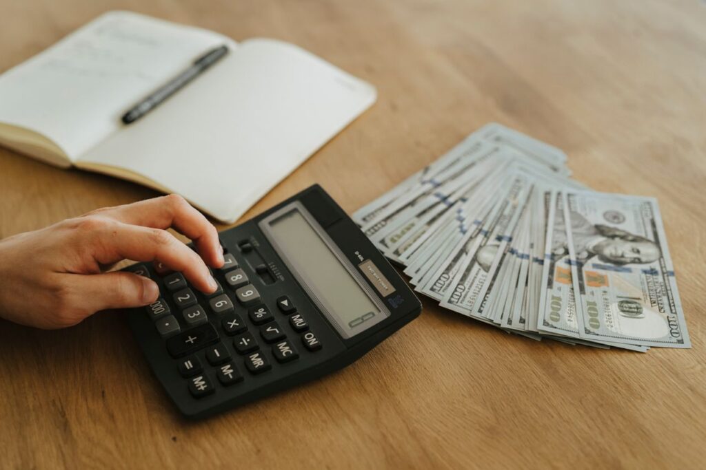 Landlord using a calculator beside cash while planning rental property maintenance and repair expenses.
