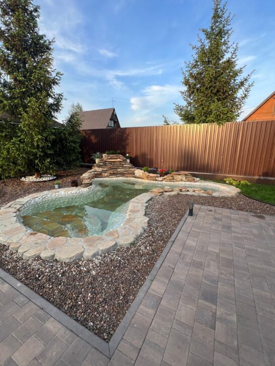 Clear backyard garden pond with stone edging, waterfall, and surrounding landscaping Do you like this personality?