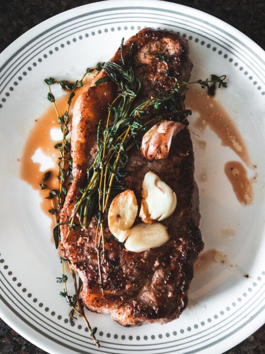 Grilled steak topped with roasted garlic and fresh herbs showing how to order steak based on preferred cut and preparation.