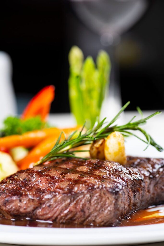 Juicy grilled steak garnished with rosemary and roasted garlic served with fresh vegetables.