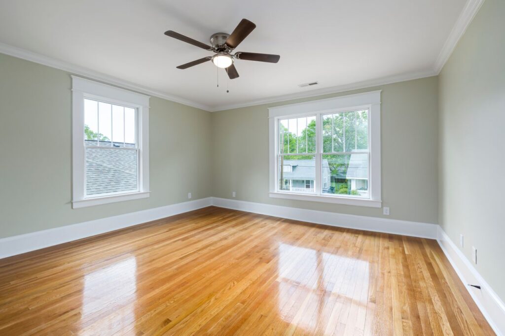 Bright empty room with polished hardwood flooring and large windows.