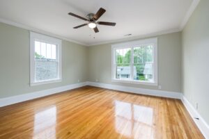 Bright empty room with polished hardwood flooring and large windows.