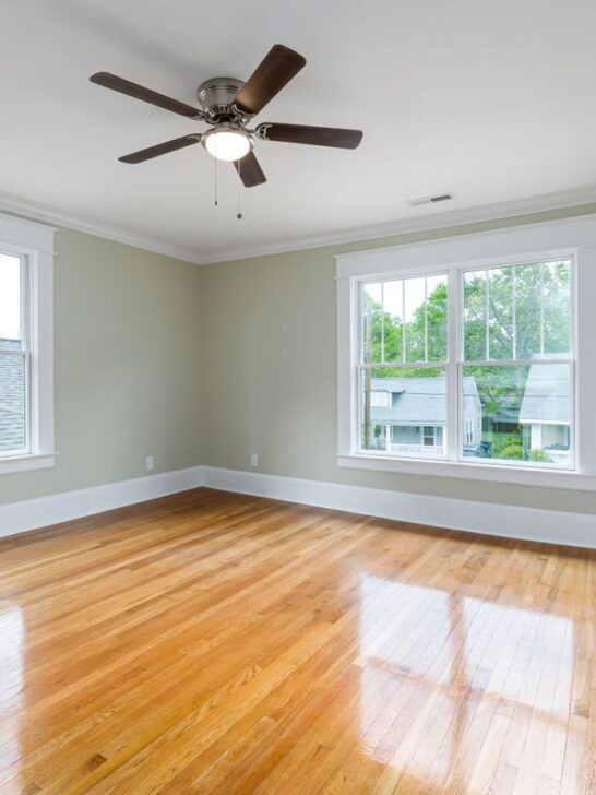 Bright empty room with polished hardwood flooring and large windows.