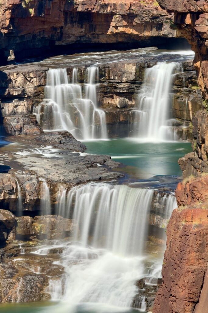 Waterfalls cascading over layered red and brown rock formations into pools below.