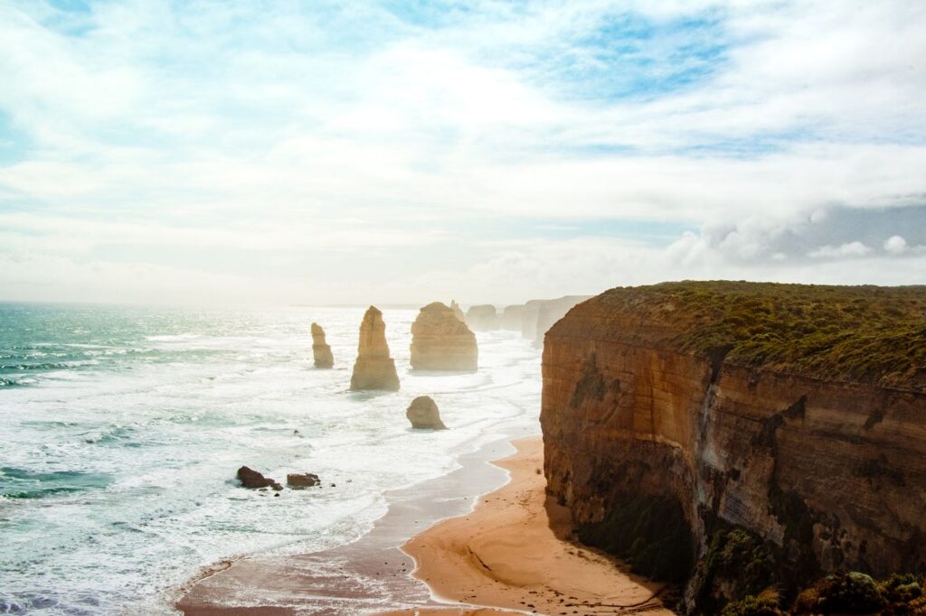 Rugged Australian coastline with towering sea stacks, sandy beach, and waves along the shore.