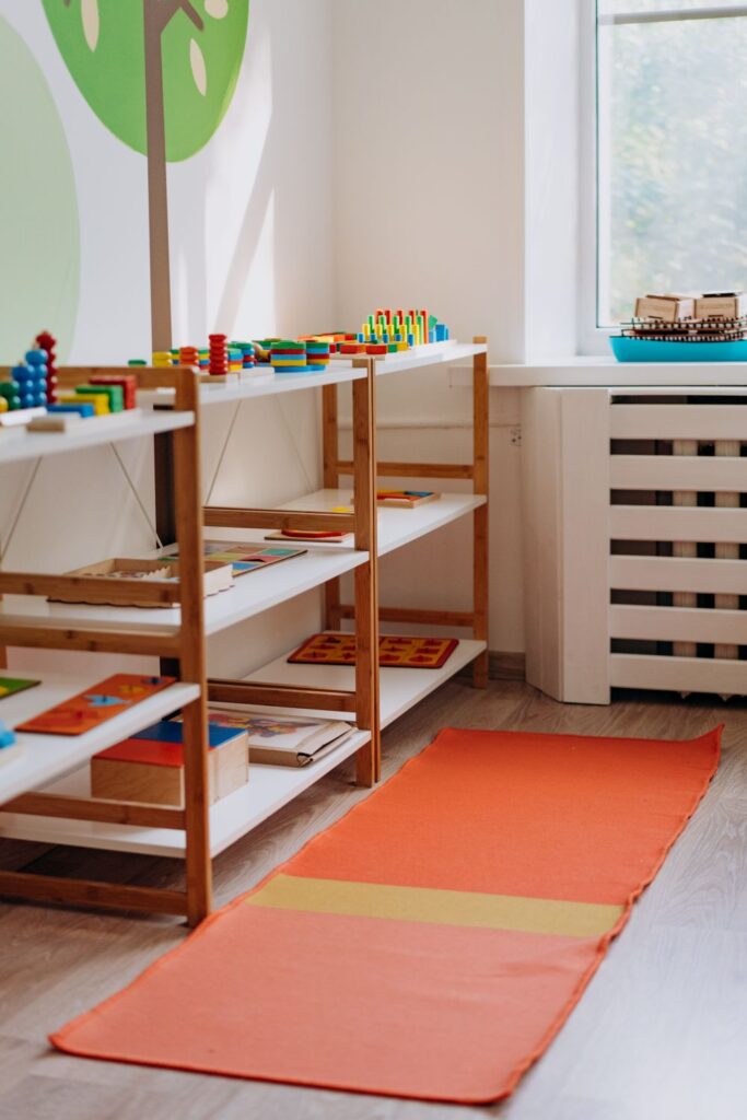 Montessori-style kindergarten classroom with colorful learning toys, activity shelves, and floor mat.