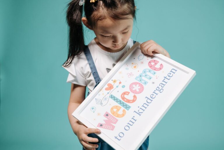Young student holding a welcome to kindergarten in Singapore sign against a blue background.