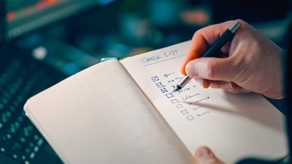 Person writing and checking off tasks on a checklist in a notebook.