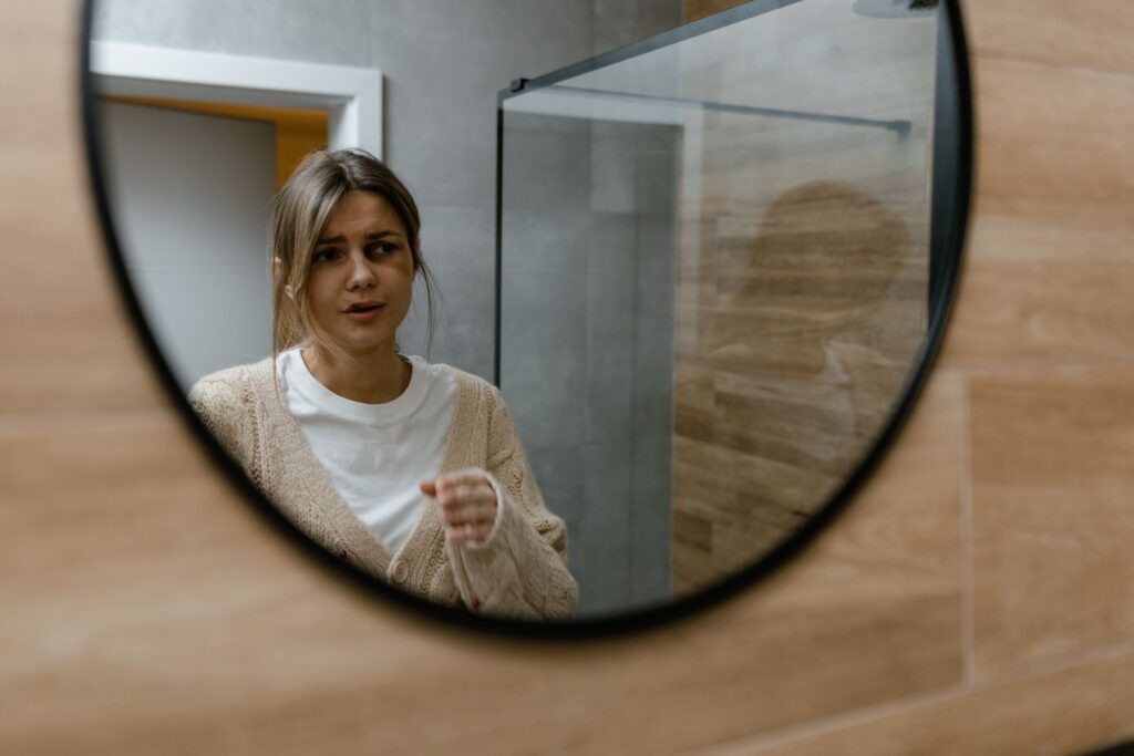Woman looking at her reflection in a mirror while considering self-confidence and appearance.