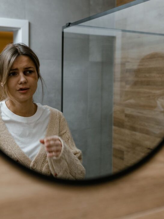 Woman looking at her reflection in a mirror while considering self-confidence and appearance.