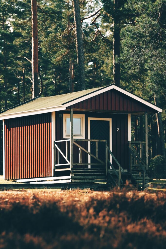 Small red shed home with a covered porch surrounded by tall trees.