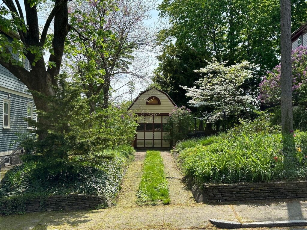 Garden pathway leading to a small outbuilding surrounded by trees and flowering plants.