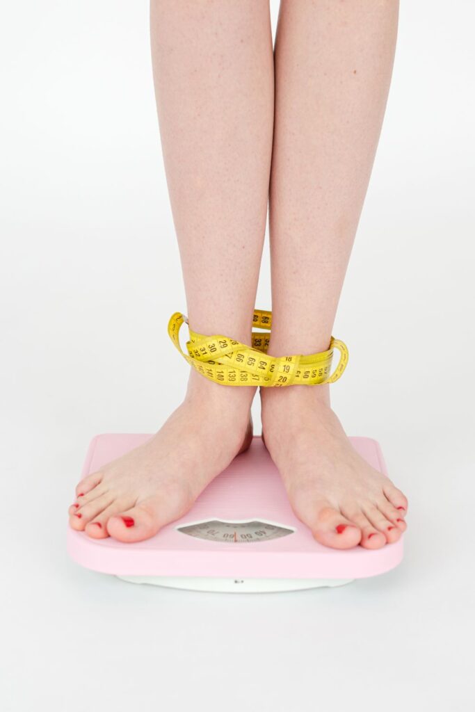 Woman standing on a scale with a measuring tape around her ankles during a weight management journey.