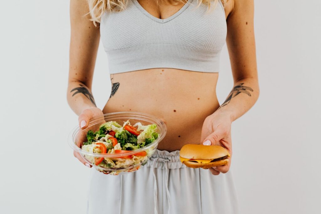 Woman holding a fresh salad in one hand and a burger in the other to represent balanced food choices.
