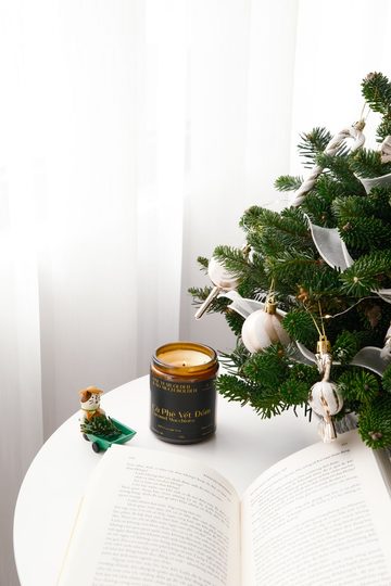 1. Christmas decorating for small spaces with a tabletop tree, white ornaments, ribbon, and a jar candle beside an open book.