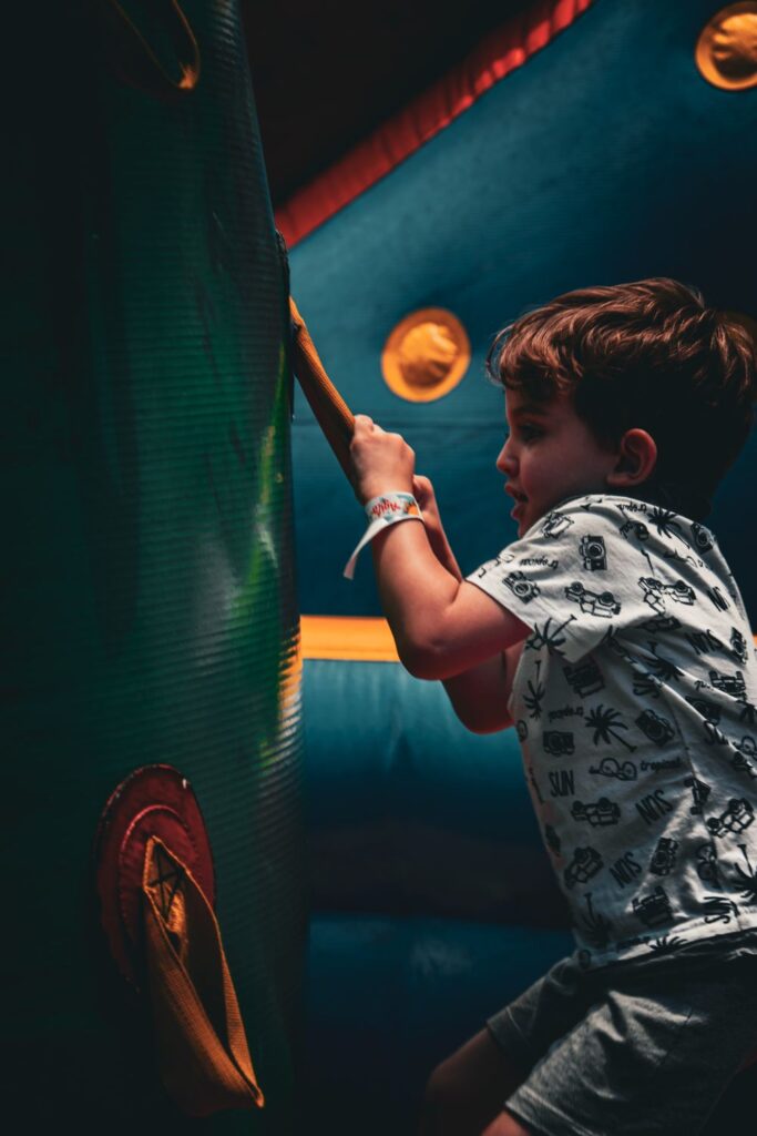 Young boy gripping an orange strap while climbing inside a teal inflatable obstacle course.
