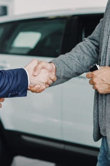 Hand holding car keys in front of a white vehicle while changing family cars.