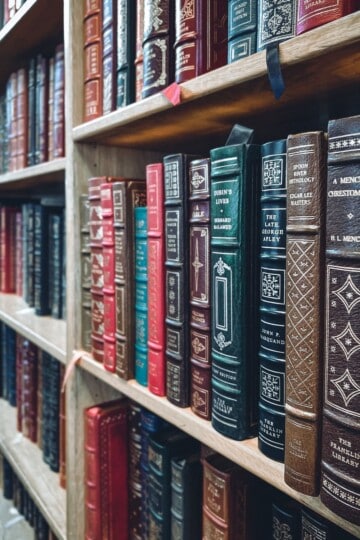 Leather-bound literature books with decorative spines on wooden shelves, illustrating resources for developing critical reading skills.