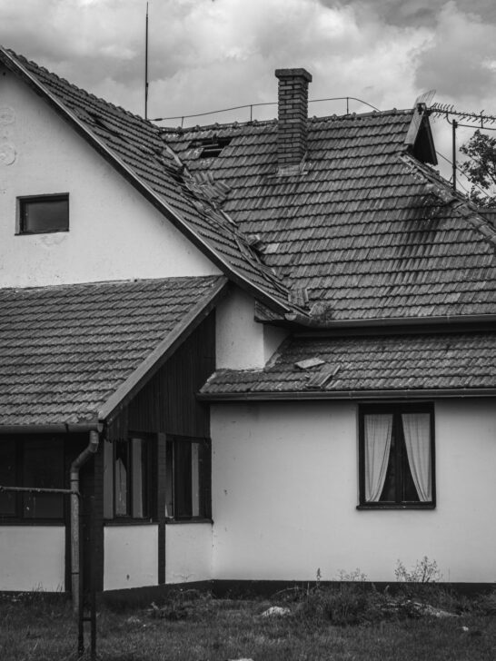Home exterior damage showing missing and displaced roof tiles on an older house.