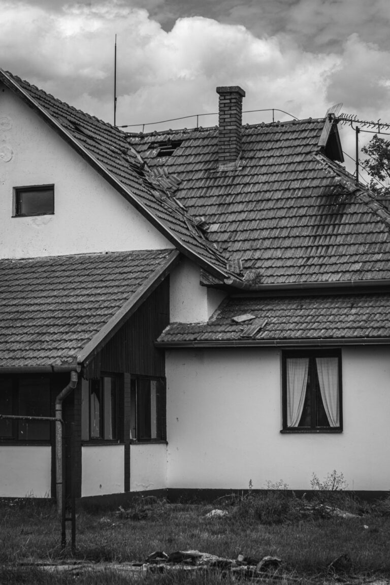 Home exterior damage showing missing and displaced roof tiles on an older house.