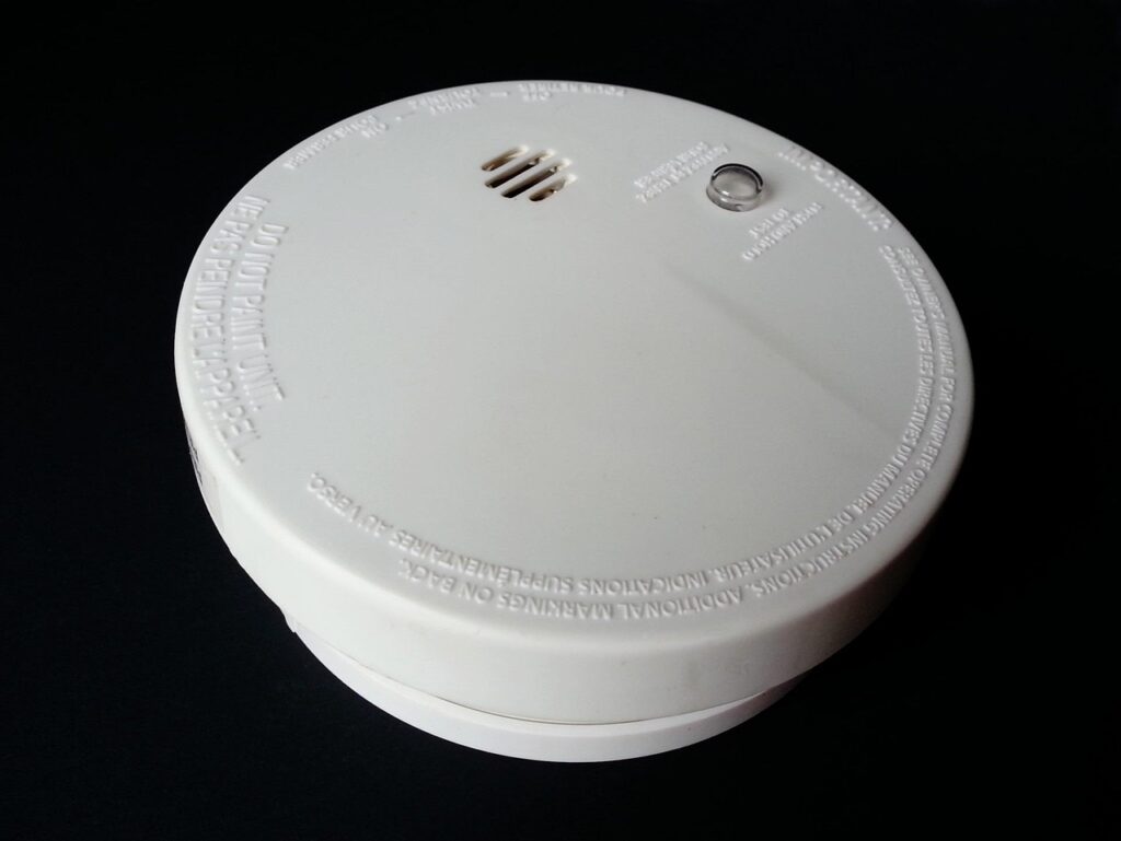 Close-up of a white smoke alarm with a test button, illustrating safety checks for home maintenance tasks.