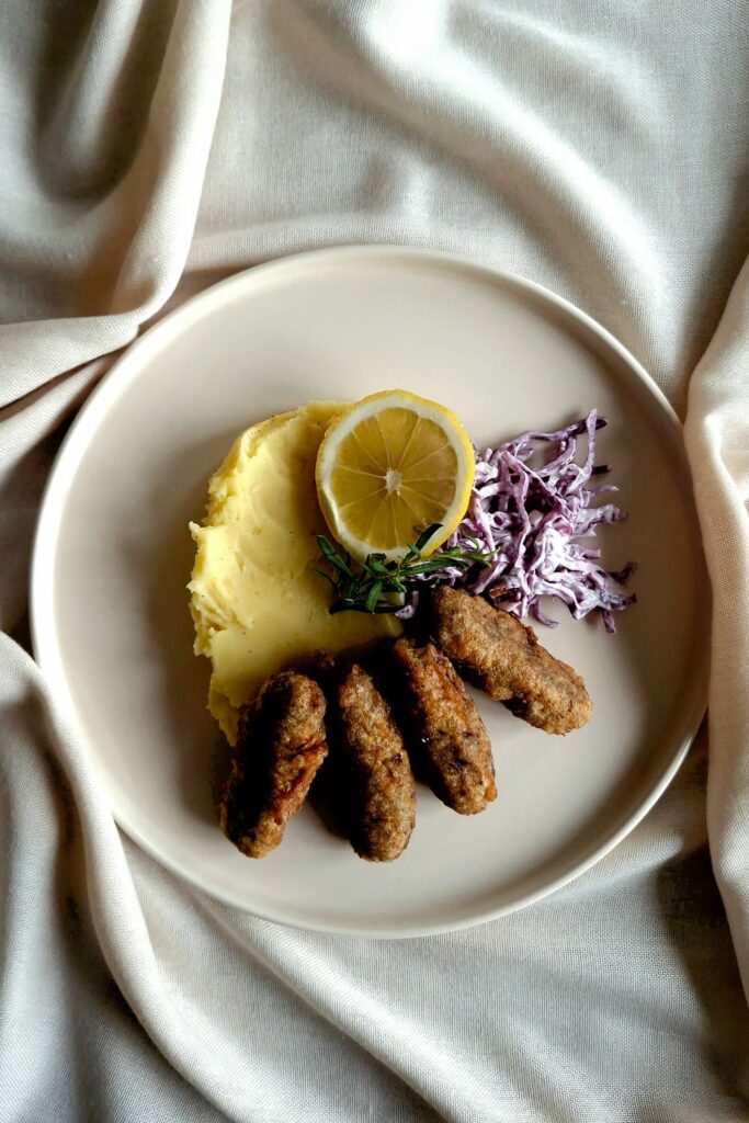 Homemade kofta kebabs served with mashed potatoes, creamy red cabbage slaw, and a lemon slice.