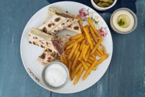 Kofta flatbread wraps served with golden fries, white dipping sauce, hummus, and pickles.