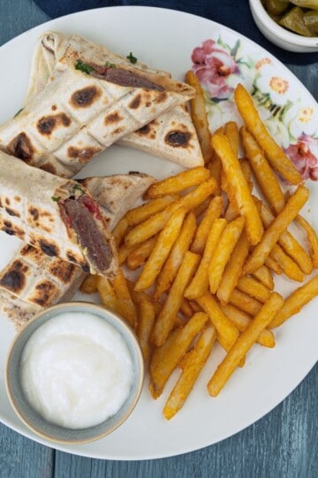 Kofta flatbread wraps served with golden fries, white dipping sauce, hummus, and pickles.