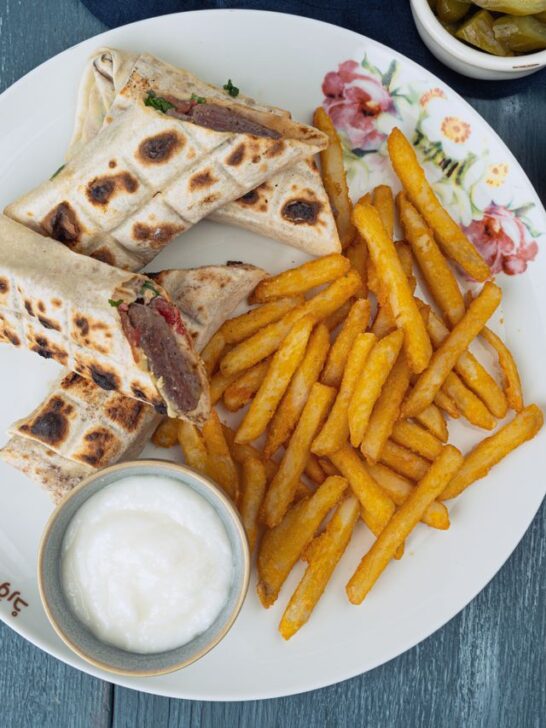 Kofta flatbread wraps served with golden fries, white dipping sauce, hummus, and pickles.