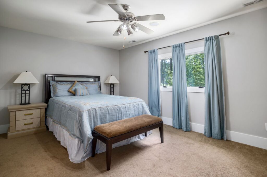 Guest bedroom with pale blue bedding, matching curtains, bedside lamps, and a cushioned bench.