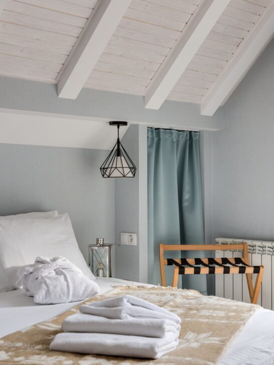 Hotel-inspired guest room ideas featuring white bedding, neatly folded towels, and a wooden luggage rack.