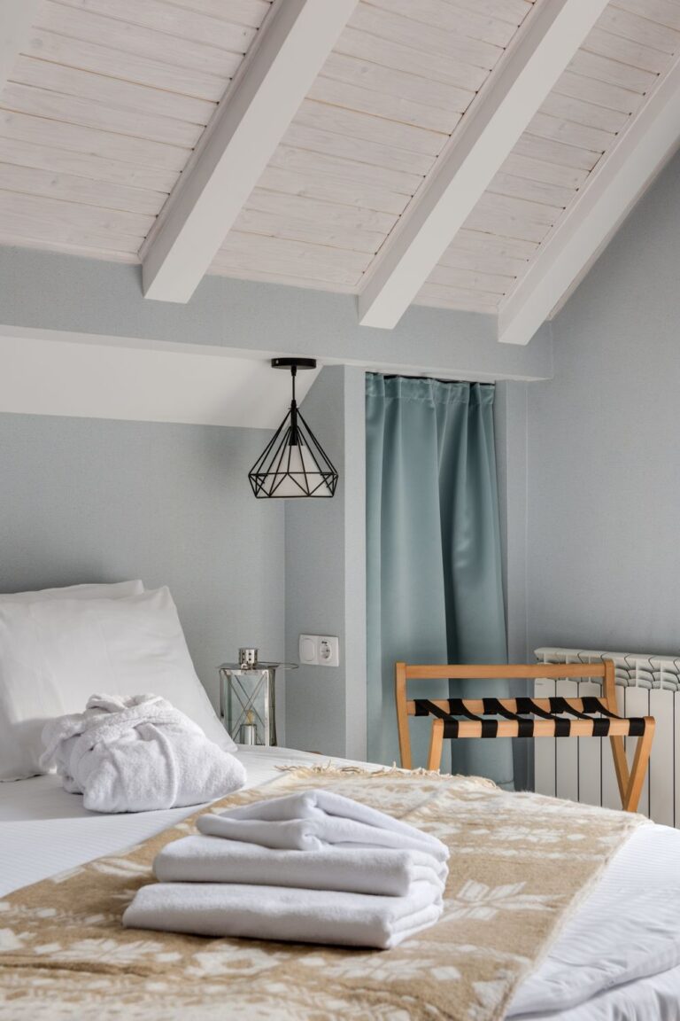 Hotel-inspired guest room ideas featuring white bedding, neatly folded towels, and a wooden luggage rack.