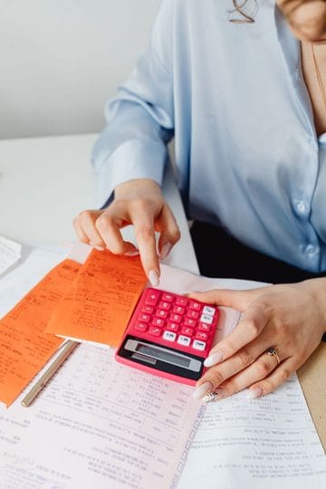 Woman using a pink calculator to total expenses beside receipts and an open notebook.