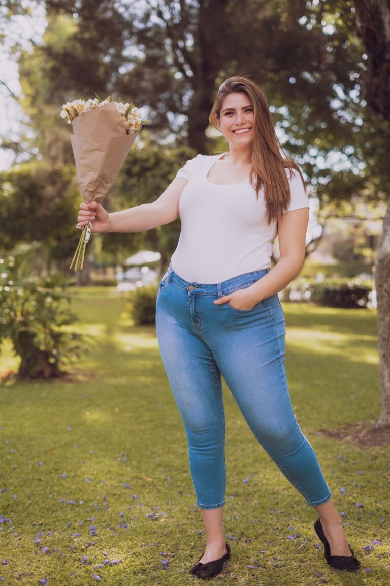 Woman wearing plus-size wardrobe staples&mdash;a white T-shirt, blue jeans, and black flats&mdash;holding a bouquet outdoors.