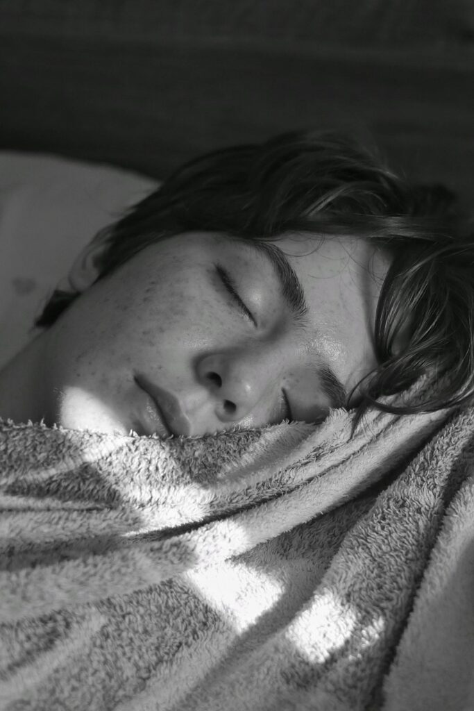 Black-and-white close-up of a person sleeping with their cheek resting on a textured blanket.