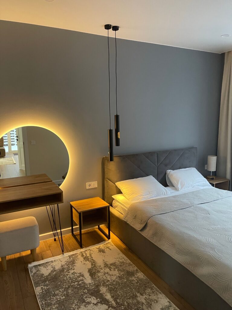 Sleep-friendly bedroom on a budget with white bedding, a gray upholstered headboard, and warm lighting.